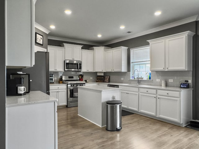 kitchen featuring appliances with stainless steel finishes, ornamental molding, a sink, backsplash, and white cabinets