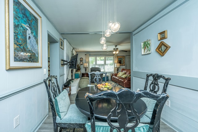 dining area with ceiling fan, wooden walls, and wood-type flooring