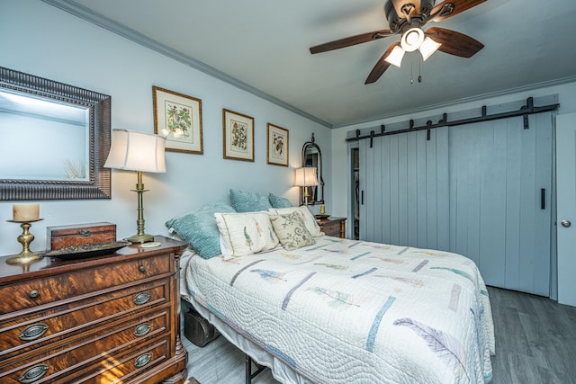 bedroom with a barn door, dark hardwood / wood-style floors, ceiling fan, and crown molding