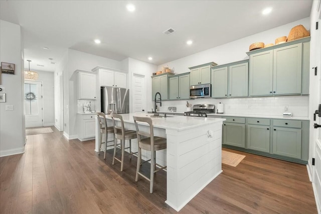 kitchen with a kitchen bar, stainless steel appliances, tasteful backsplash, an island with sink, and sink