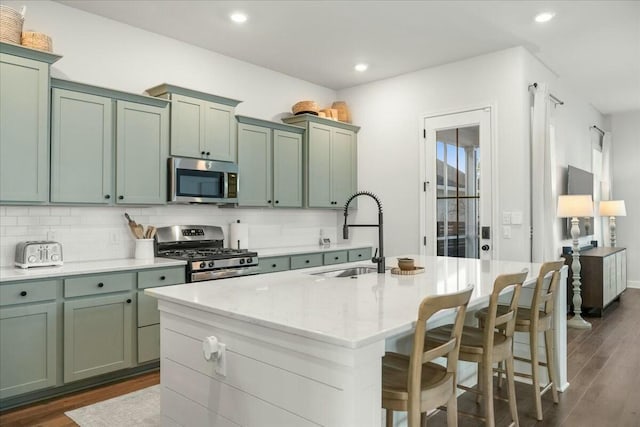 kitchen featuring stainless steel appliances, sink, a kitchen island with sink, light stone counters, and green cabinets