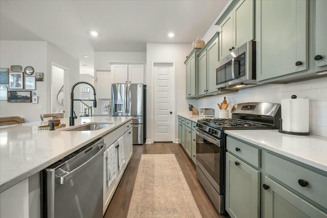 kitchen with green cabinets, stainless steel appliances, dark wood-type flooring, light stone counters, and sink