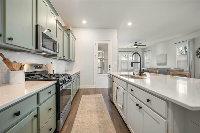 kitchen featuring ceiling fan, decorative backsplash, sink, appliances with stainless steel finishes, and an island with sink