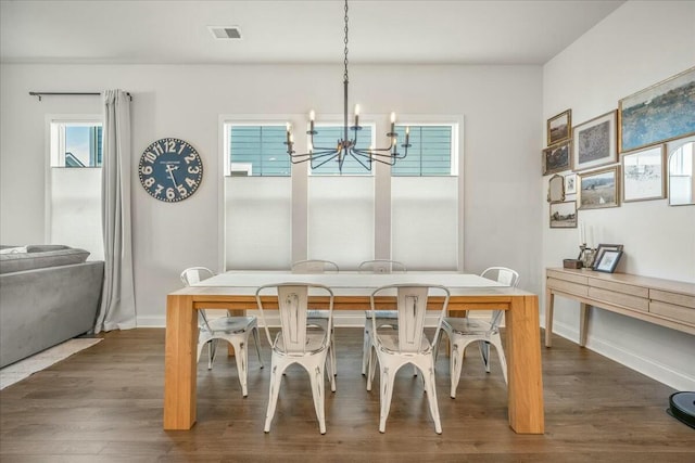 dining area with dark wood-type flooring and an inviting chandelier