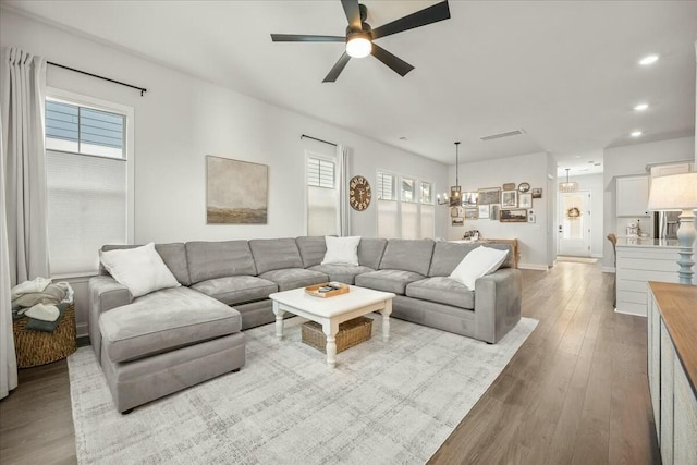 living room with light wood-type flooring and ceiling fan with notable chandelier