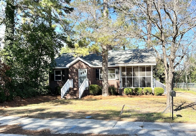 ranch-style house featuring brick siding, a front lawn, and a sunroom