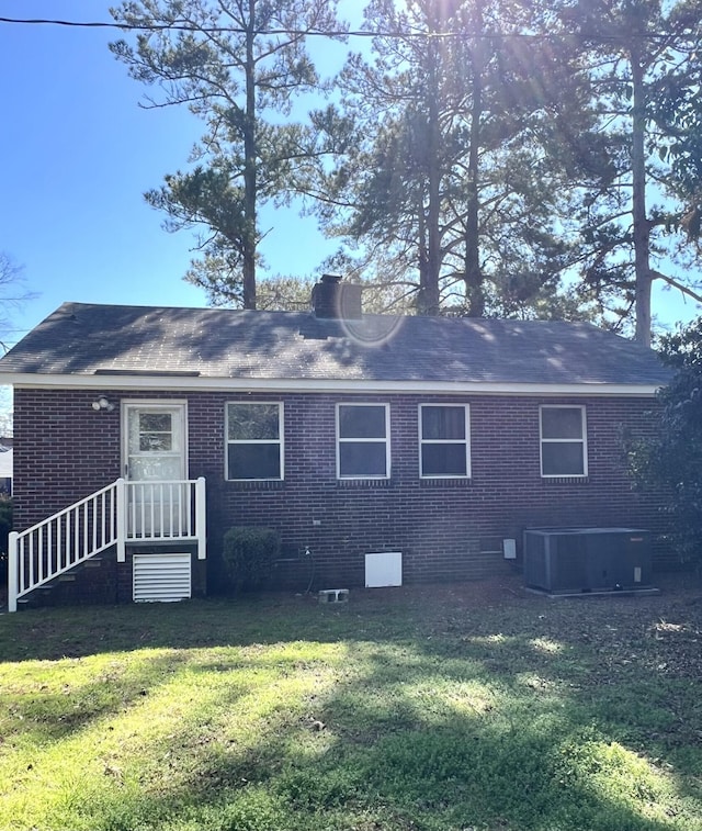 back of house featuring a yard, a chimney, central AC unit, and brick siding