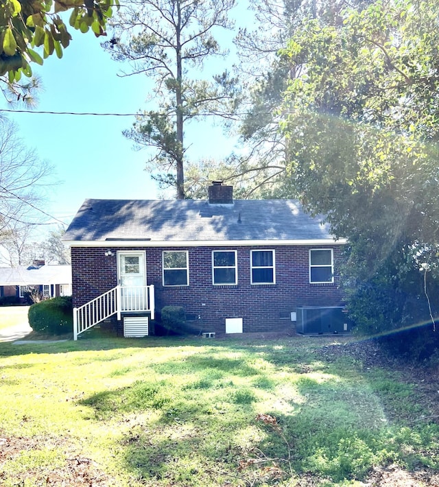 view of front of home featuring cooling unit, brick siding, a chimney, and a front lawn