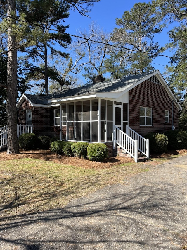 view of front of property with a sunroom, brick siding, and a chimney