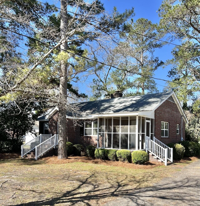 ranch-style house with a sunroom, a chimney, stairway, and brick siding