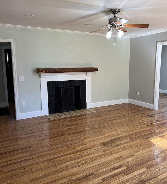 unfurnished living room with a brick fireplace, crown molding, baseboards, and wood finished floors