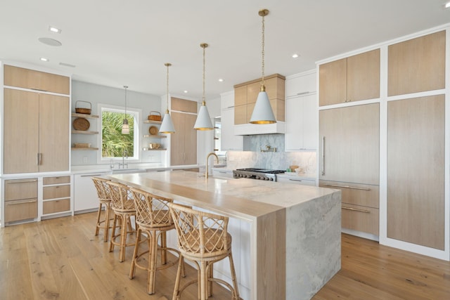 kitchen with pendant lighting, a center island with sink, light hardwood / wood-style flooring, and white cabinetry