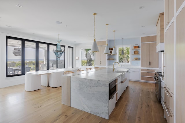 kitchen featuring white cabinetry, hanging light fixtures, light stone counters, a center island with sink, and light wood-type flooring