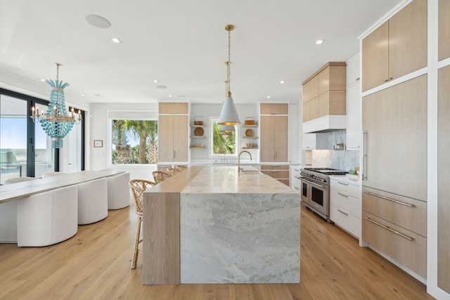 kitchen featuring light hardwood / wood-style floors, double oven range, hanging light fixtures, and a kitchen island with sink