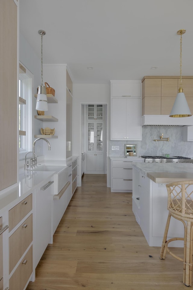 kitchen featuring sink, white cabinets, decorative light fixtures, and light wood-type flooring