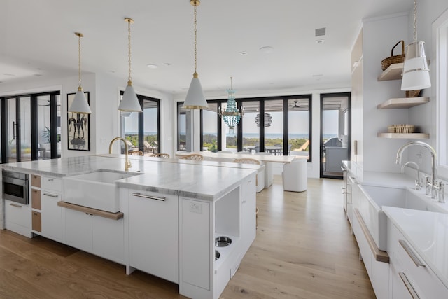 kitchen with sink, white cabinetry, an island with sink, and a wealth of natural light