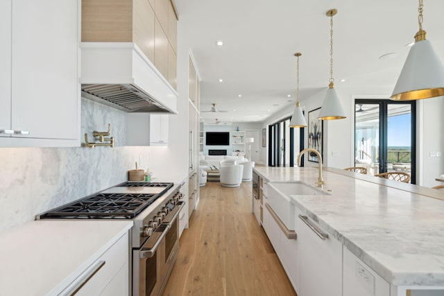 kitchen with sink, decorative light fixtures, a kitchen island with sink, high end range, and light wood-type flooring