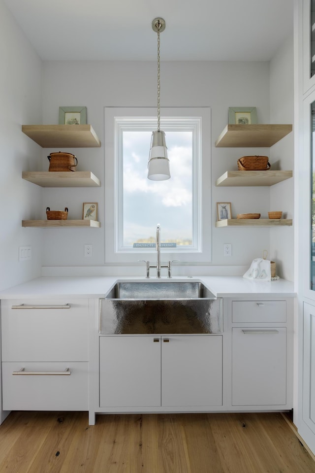 kitchen with sink, white cabinets, decorative light fixtures, and light wood-type flooring