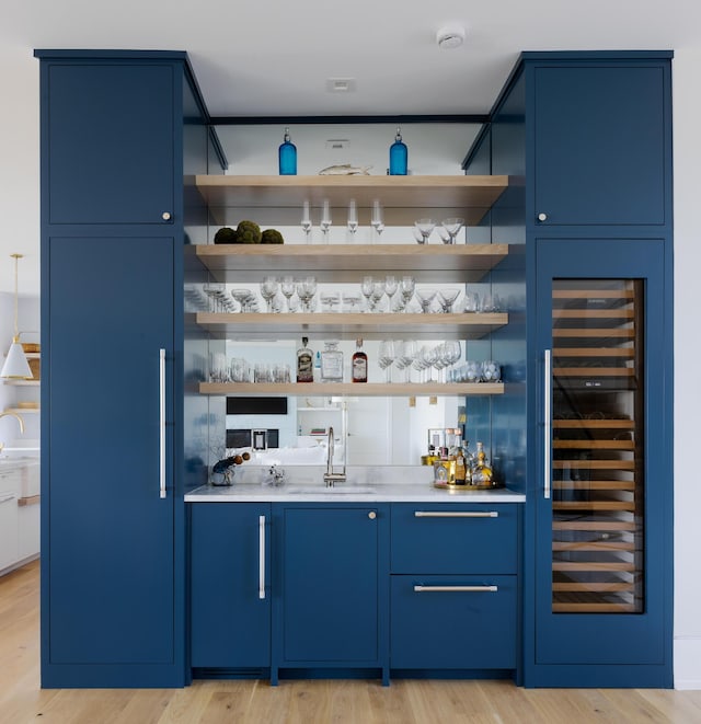 bar with light hardwood / wood-style floors, blue cabinets, and wine cooler