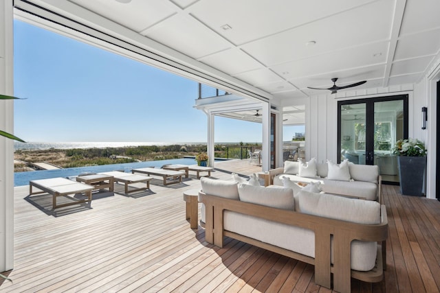 wooden deck featuring an outdoor living space, ceiling fan, and a water view