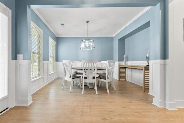 dining room featuring light wood finished floors, wainscoting, an inviting chandelier, crown molding, and a decorative wall