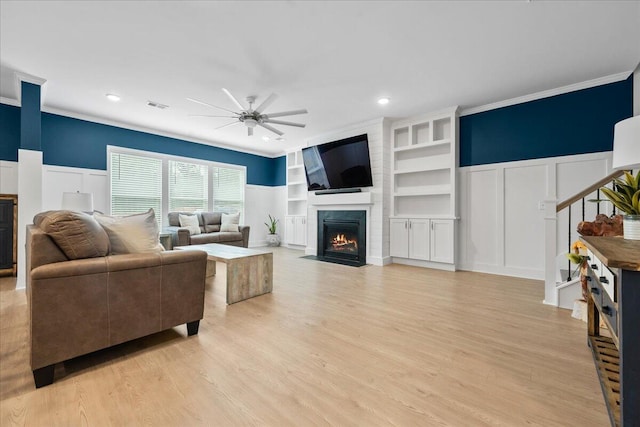 living room with built in shelves, a fireplace, visible vents, light wood-style floors, and ceiling fan