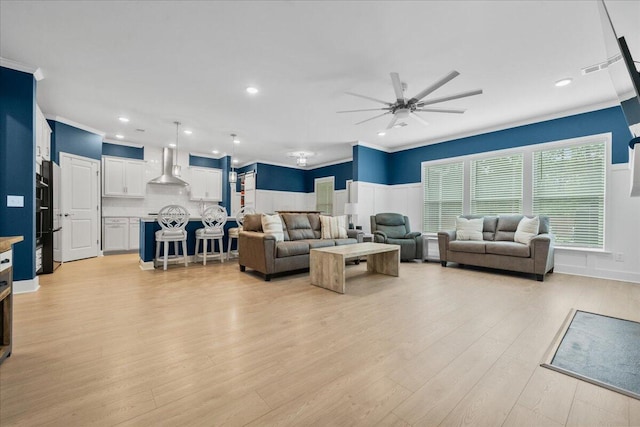 living room featuring a wainscoted wall, ornamental molding, a ceiling fan, and light wood-style floors