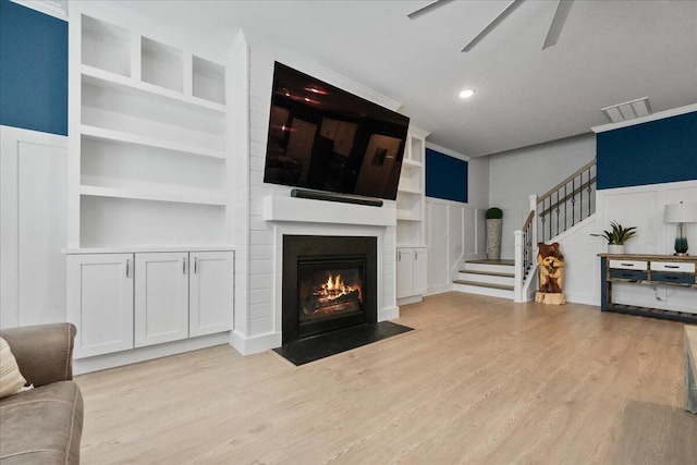 living area featuring a large fireplace, stairs, crown molding, light wood-type flooring, and built in shelves