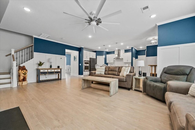 living room with stairway, light wood-style flooring, visible vents, and crown molding