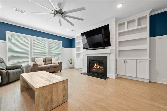 living area with built in features, a fireplace, visible vents, ceiling fan, and light wood-type flooring