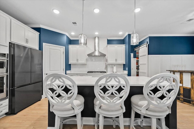 kitchen with light countertops, a barn door, light wood-style floors, freestanding refrigerator, and wall chimney range hood