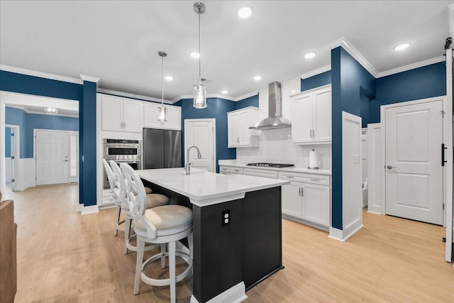 kitchen featuring stainless steel appliances, a breakfast bar, a sink, light countertops, and wall chimney exhaust hood