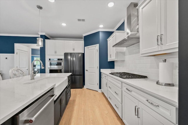 kitchen with stainless steel appliances, wall chimney range hood, a sink, and white cabinetry