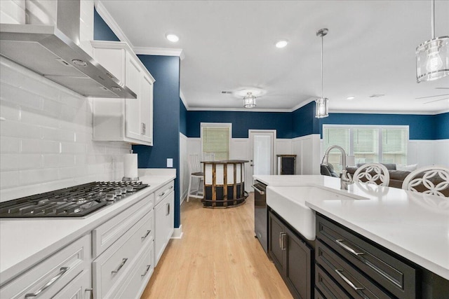 kitchen featuring light countertops, stainless steel gas stovetop, white cabinets, a sink, and wall chimney exhaust hood