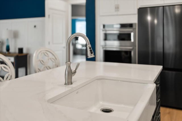 room details featuring white cabinets, a wainscoted wall, freestanding refrigerator, stainless steel double oven, and a sink