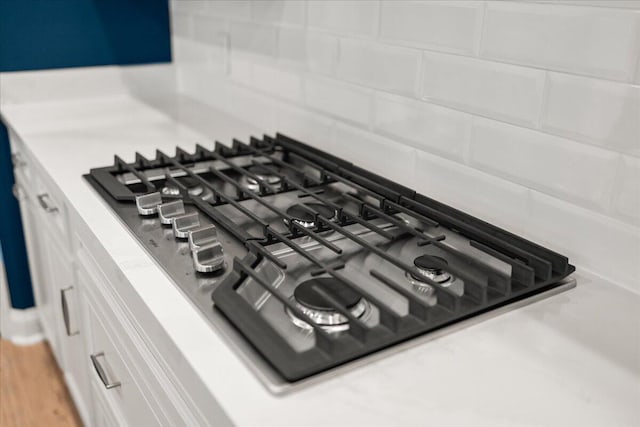 details featuring white cabinets, stainless steel gas cooktop, light countertops, and backsplash