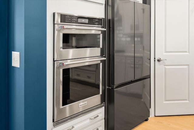 kitchen featuring stainless steel double oven, freestanding refrigerator, and light wood-style floors