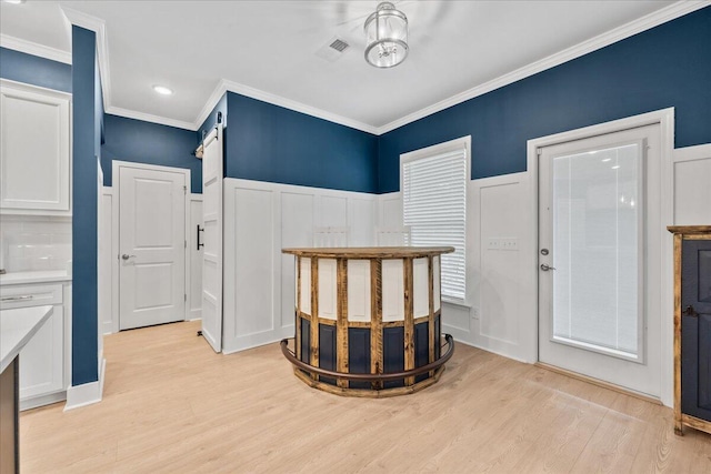 interior space featuring visible vents, wainscoting, crown molding, light wood-type flooring, and a decorative wall