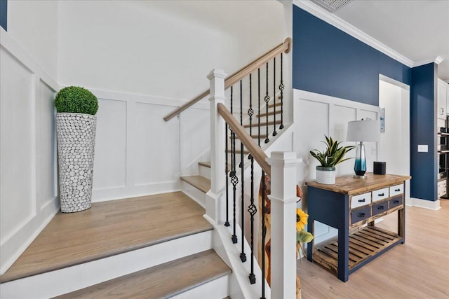 stairway featuring ornamental molding, wood finished floors, and a decorative wall