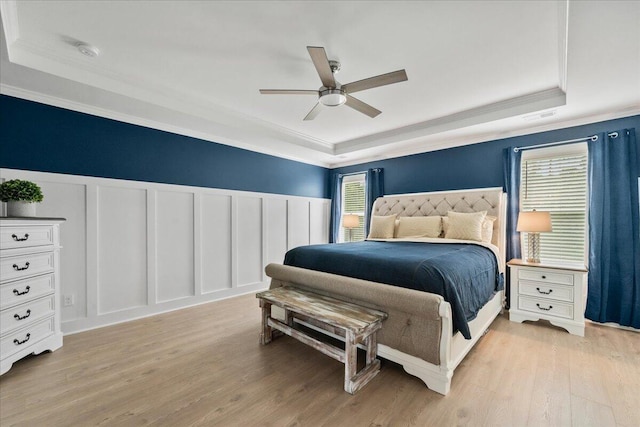 bedroom with a raised ceiling, multiple windows, and a decorative wall