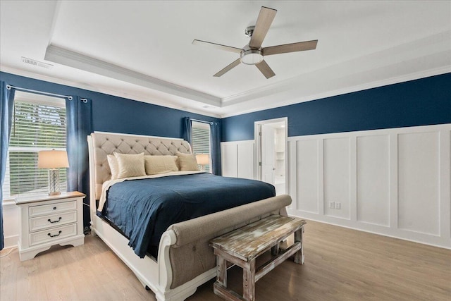 bedroom featuring crown molding, light wood-type flooring, a raised ceiling, and a decorative wall