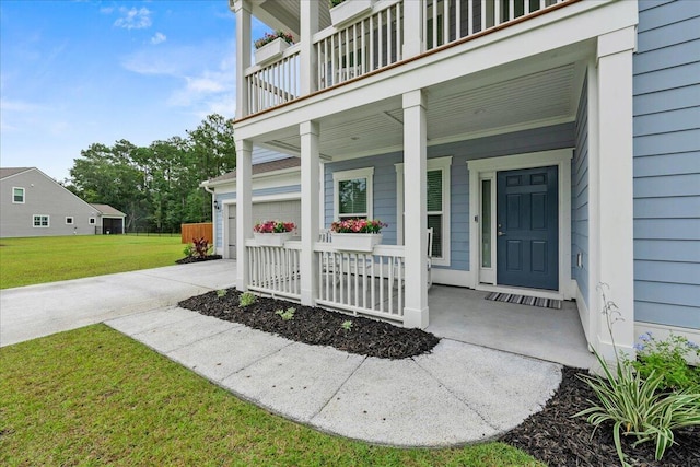 view of exterior entry featuring a yard, a porch, concrete driveway, a balcony, and a garage