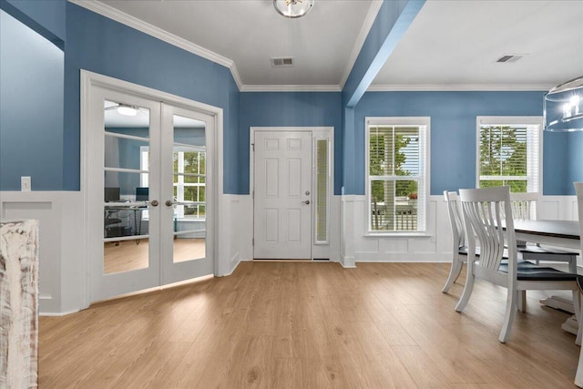 foyer entrance with visible vents, a wainscoted wall, light wood-style flooring, ornamental molding, and french doors