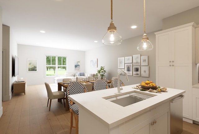 kitchen featuring a kitchen island with sink, light wood-type flooring, sink, hanging light fixtures, and white cabinets