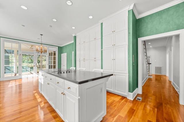 kitchen with light wood-type flooring, french doors, a center island, white cabinets, and decorative light fixtures