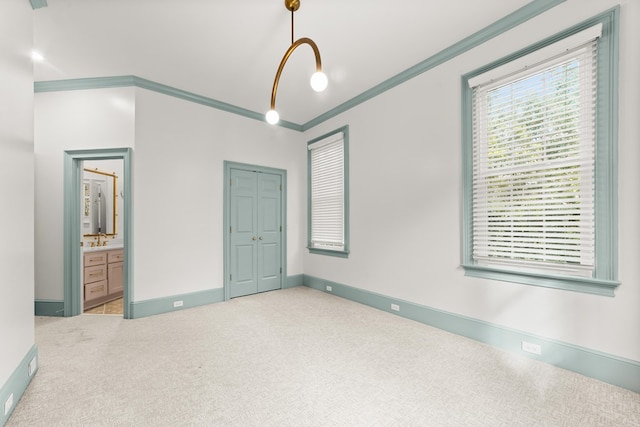 unfurnished bedroom featuring a closet, crown molding, ensuite bath, and light carpet