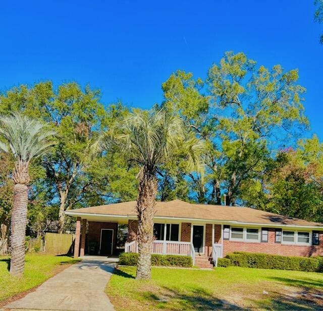 single story home featuring a front yard, covered porch, an attached carport, and concrete driveway