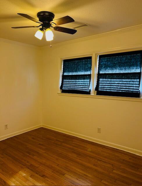 empty room featuring ornamental molding, baseboards, and dark wood finished floors