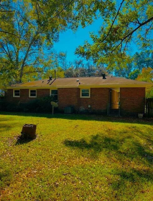 rear view of property featuring brick siding, central AC unit, and a lawn