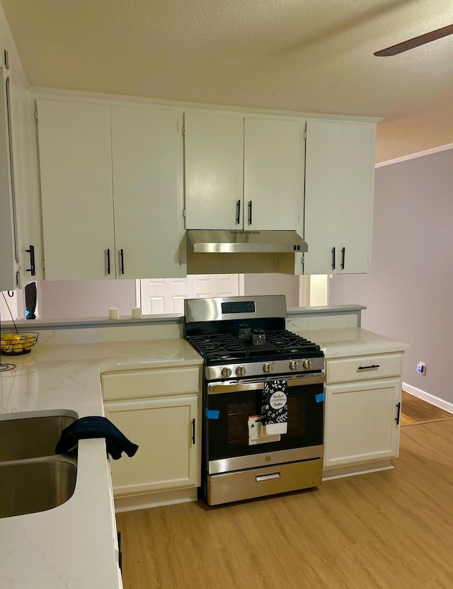 kitchen featuring gas stove, a textured ceiling, under cabinet range hood, light wood-style floors, and ceiling fan